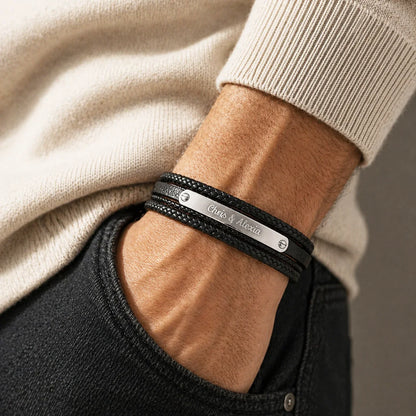 Bracelet cuir noir multi-brins avec plaque acier gravée, porté au poignet, pull écru